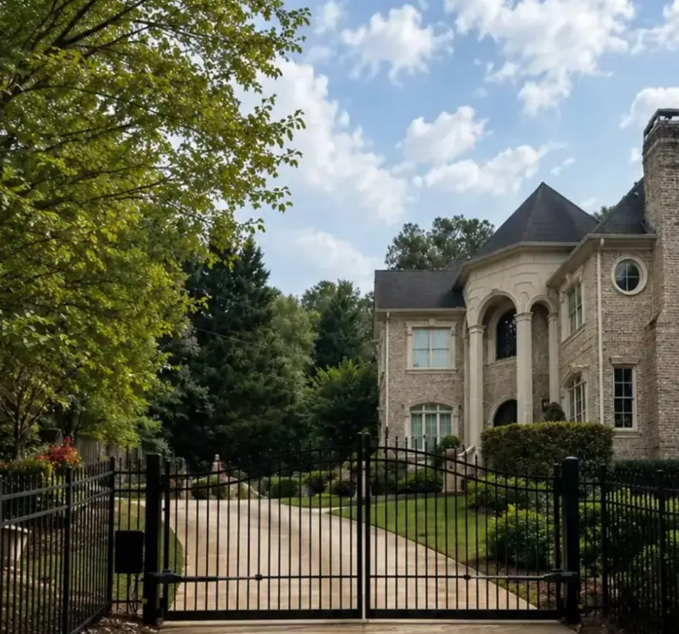 Ornamental steel driveway gate and fence in front of a brick Georgia home